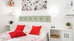 Een keurig opgemaakt slaapkamer met een bed, kussens, een schilderij, een gestreept hoofdeinde en opbergmeubels.