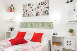 Ein aufgeräumtes Schlafzimmer mit einem Bett, Kissen, einem Gemälde, einem gemusterten Kopfteil und Stauraumelementen.