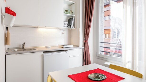 Een compacte keuken met een spoelbak, vaatwasser en een eethoek met een tafel en stoelen.