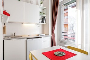 A compact kitchen with a sink, dishwasher, and a dining area with a table and chairs. - Guesthost - Fortezza Functional Studio (Florence)