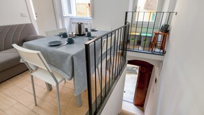 A dining area with a table set for four, a sofa, and a staircase leading to an upper level. - Guesthost - La Cantina Dei Nonni - Riomaggiore Functional Flat (Riomaggiore)