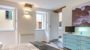 A bedroom with a bed, a dresser, a television, and a painting on the wall. - Guesthost - La Cantina Dei Nonni - Riomaggiore Functional Flat (Riomaggiore)