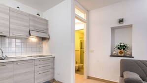 A modern kitchen with light wood cabinets, a built-in oven, and a sink. There is a gray sofa with a cushion and a small plant on a shelf. - Guesthost - La Cantina Dei Nonni - Riomaggiore Functional Flat (Riomaggiore)