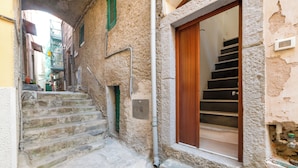 A narrow stone staircase leading to a wooden door, with a small window and a metal pipe on the wall. - Guesthost - La Cantina Dei Nonni - Riomaggiore Functional Flat (Riomaggiore)
