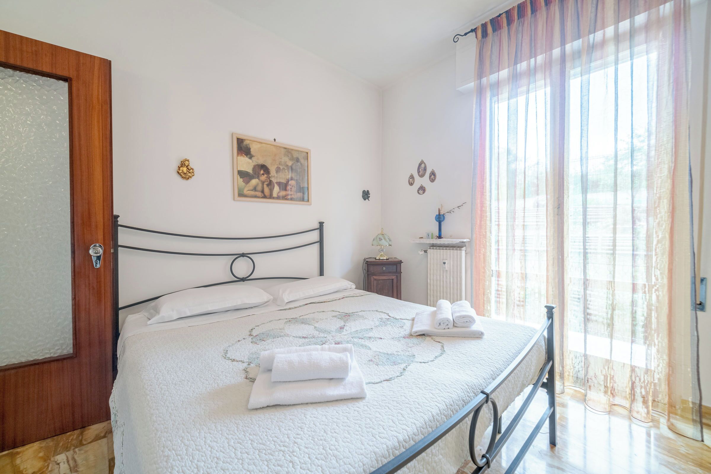 A bedroom with a bed, a nightstand, a lamp, and a window with curtains.