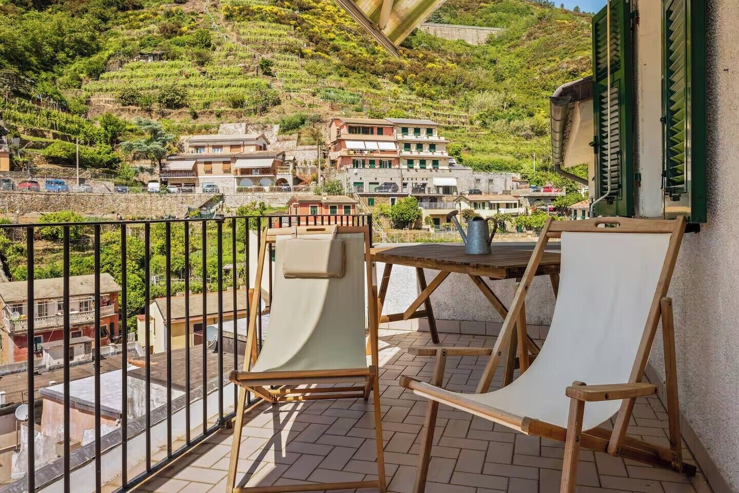 A balcony with two chairs and a table, overlooking a hillside with buildings.