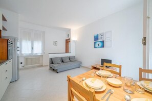 Eine moderne Küche mit weißen Schränken, einem Esstisch für vier Personen und einem grauen Sofa im Wohnbereich.