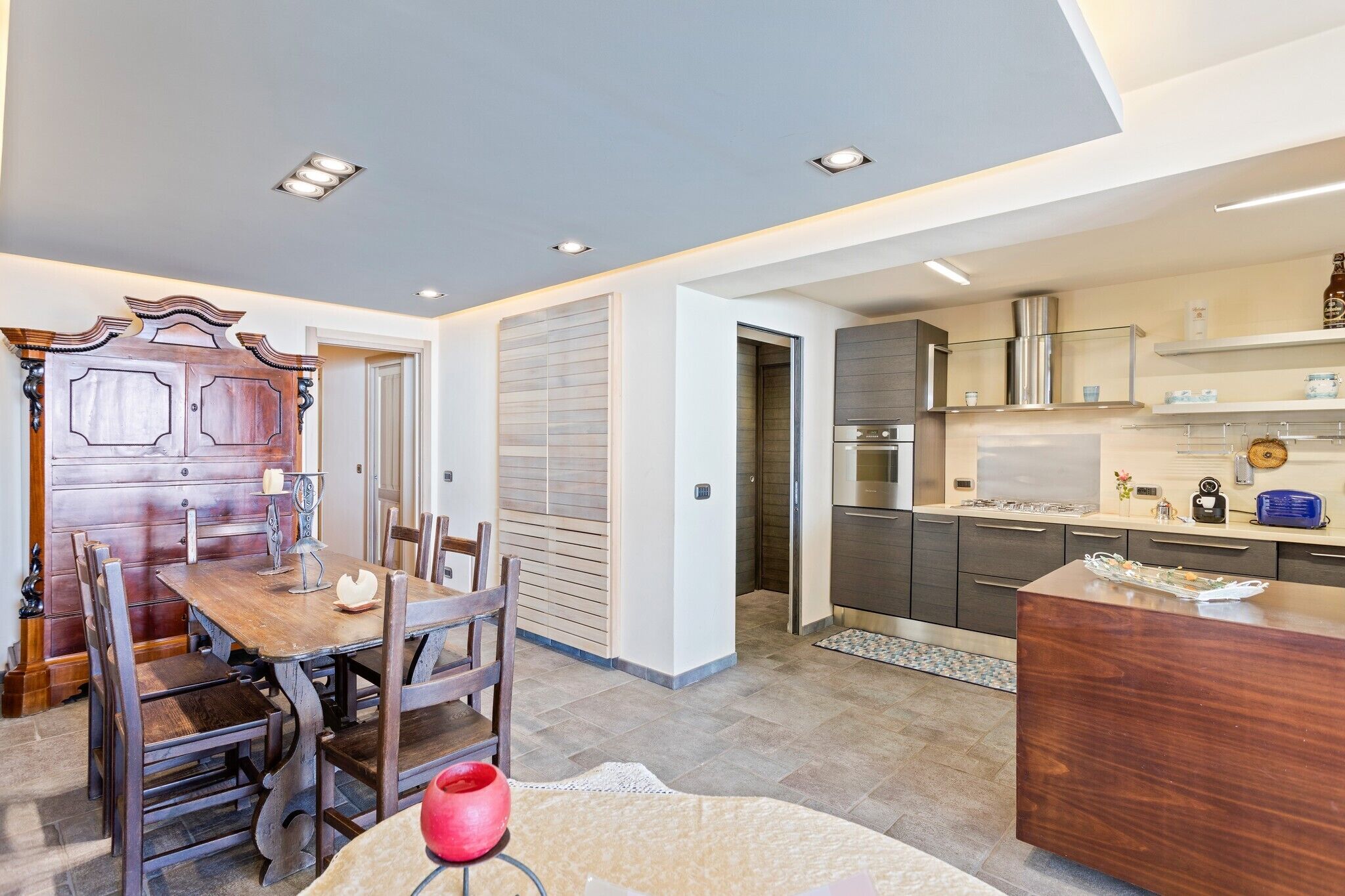 A modern kitchen with a built-in oven, a dining area with a wooden table and chairs, and a separate dining room with a wooden cabinet.