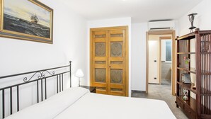 Ein Schlafzimmer mit einem Bett, einem Holzschrank, einem Bücherregal, einem Gemälde und einer Tür zu einem anderen Raum.