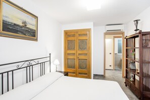 A bedroom with a bed, a wooden wardrobe, a bookshelf, a painting, and a door leading to another room. - Guesthost - Penelope Seaview Apartment (Catania)