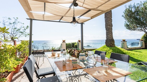 Eine Terrasss mit Glastisch, Stühlen und Meerblick.