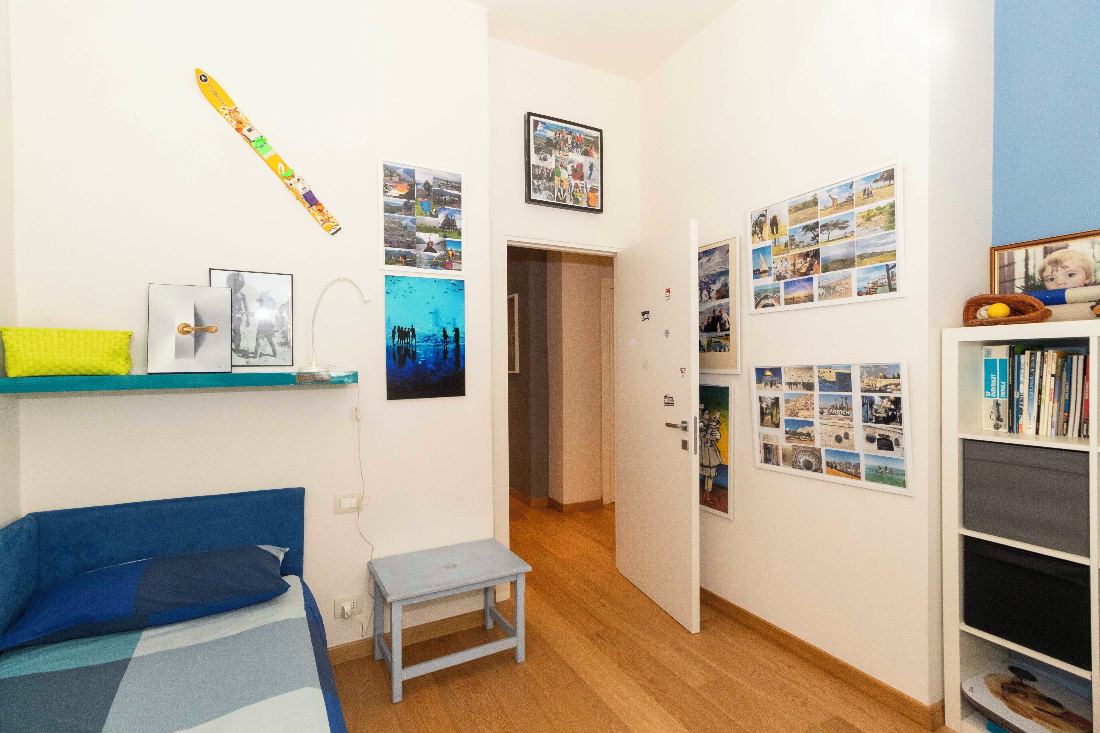 Une pièce comprenant un lit, une petite table, une bibliothèque et divers tableaux encadrés accrochés aux murs.