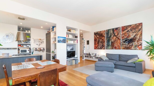 Ein moderner Wohnraum mit Essbereich, grauem Sofa und einem großen abstrakten Gemälde.