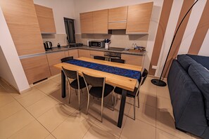 A compact kitchen with wooden cabinets, a microwave, and a dining area with a table and chairs. - Cobalt Canopy – Spacious 2-Bedroom Apartment (San Pawl il-Baħar (Qawra))