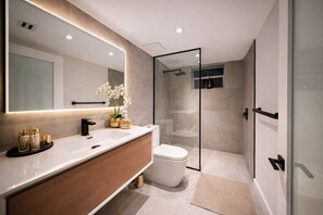 A modern bathroom with a large mirror, a vanity with a sink, a toilet, and a glass-enclosed shower area. - The Rose By Brickell (Miami)