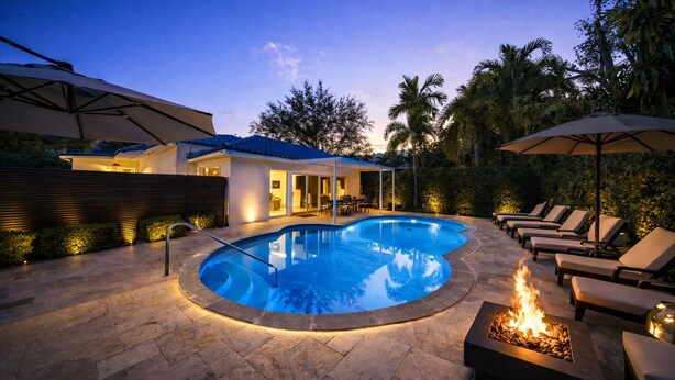 Ein Pool mit Feuerstelle, umgeben von Liegestühlen und einer überdachten Sitzgruppe.