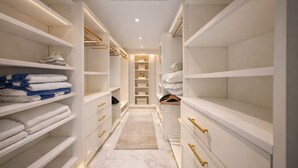 Ein begehbarer Kleiderschrank mit weißen Regalen, goldenen Griffen und einem Marmorboden.