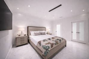 A modern bedroom with a large bed, bedside tables with lamps, a flat-screen TV, and a wardrobe with glass doors. - The Rose By Brickell (Miami)