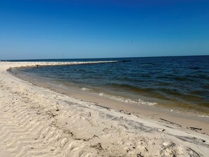A sandy beach with gentle waves, a clear sky, and a distant pier. - Beach View Condo Long Beach, MS (Long Beach)