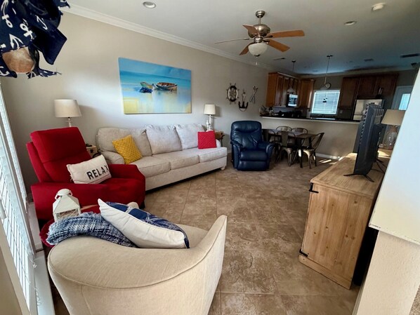 A living room with a sofa, a red armchair, a blue chair, a wooden cabinet, and a dining area with a table and chairs. - Beach View Condo Long Beach, MS (Long Beach)