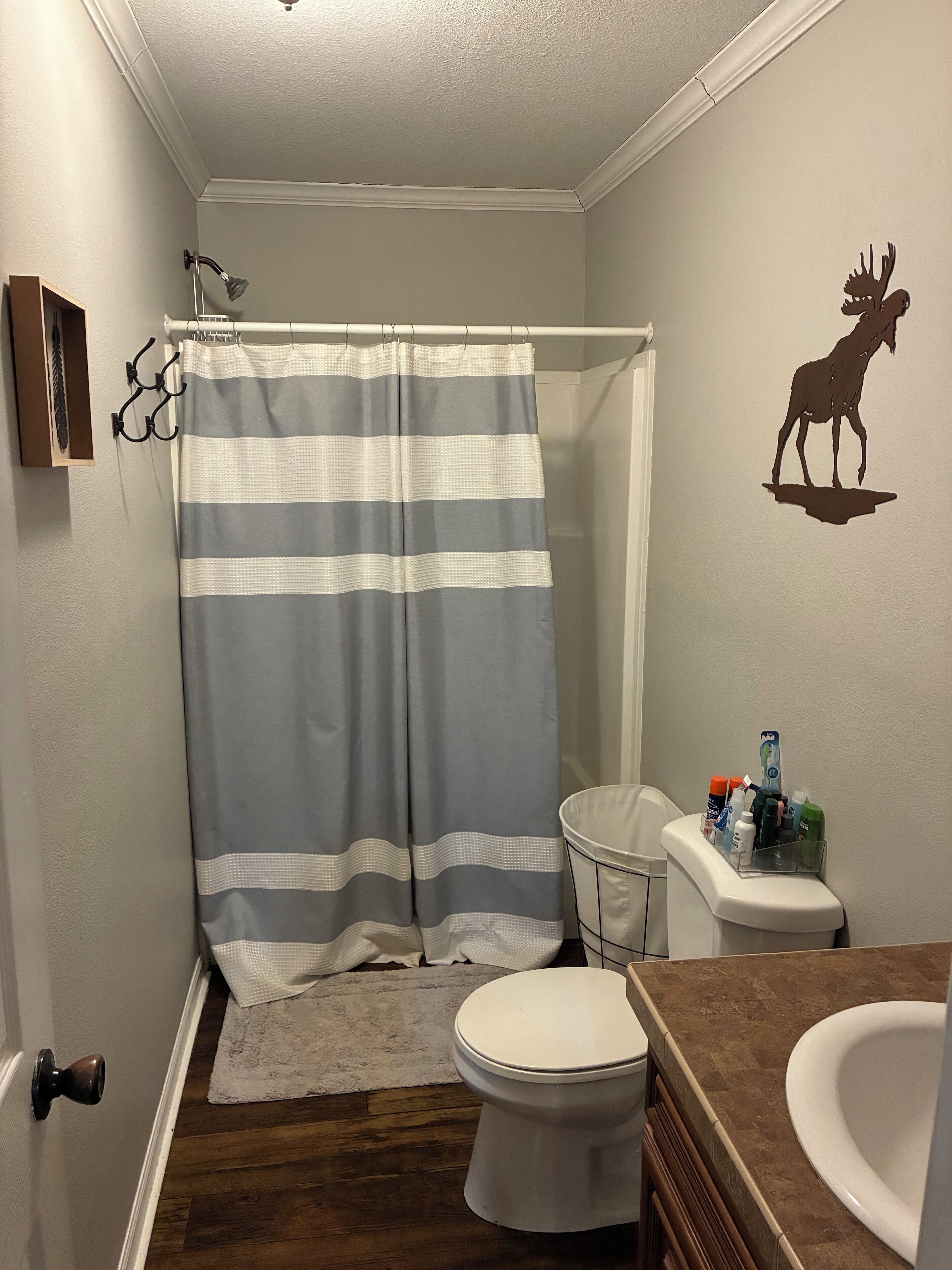 A bathroom with a shower curtain, toilet, sink, and a wall decal of a moose.