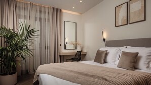 Una habitación de hotel moderna con una cama grande, un escritorio, una planta en maceta y cuadros en la pared.