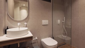 Un baño moderno con un espejo redondo, un lavamanos blanco y una ducha con cerramiento de vidrio.