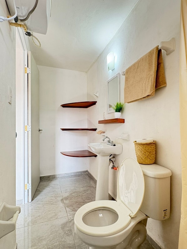 A bathroom with a toilet, a sink, and a mirror. There are wooden shelves above the sink and a towel hanging on the wall. - Monet Hotel Motul (Motul)