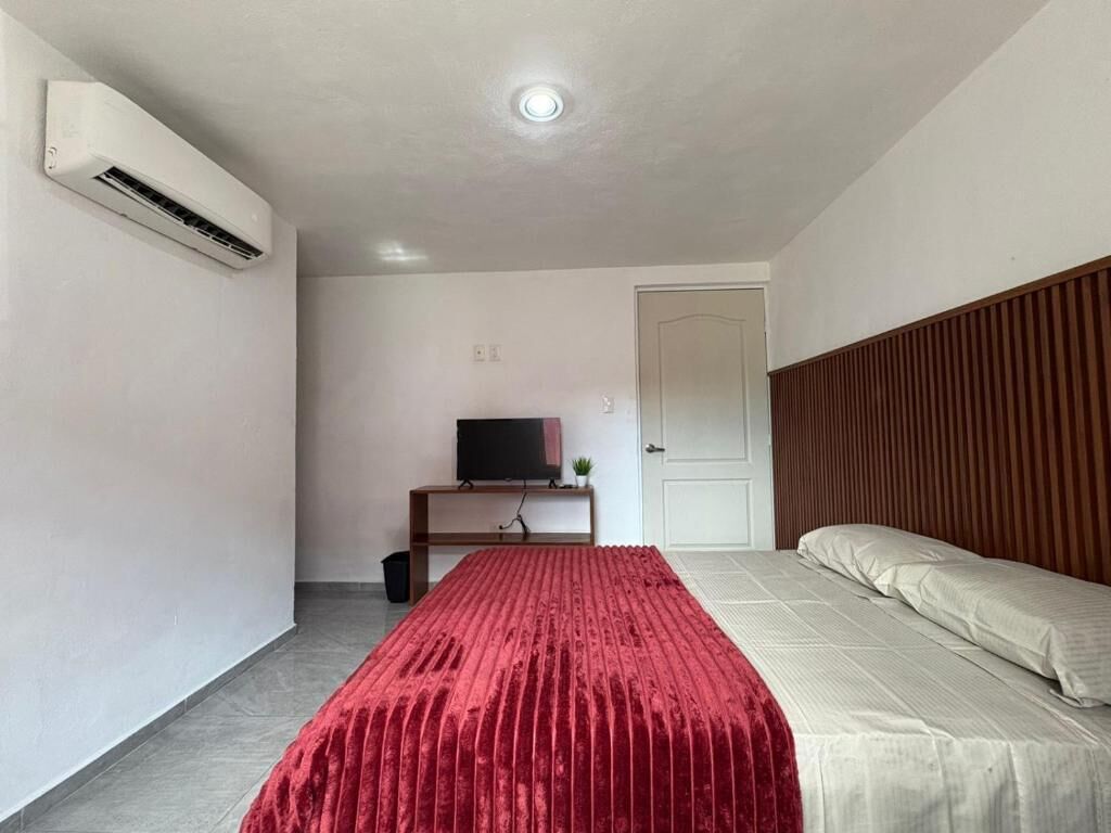 A bedroom with a bed, a TV on a stand, and an air conditioning unit.
