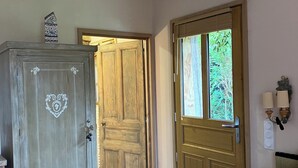 Une chambre avec une armoire en bois, un lit avec un oreiller à carreaux et une fenêtre donnant sur un paysage verdoyant.
