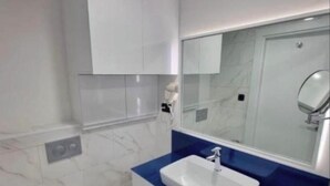 Casa de banho moderna com sanita branca, toucador azul e um espelho grande.