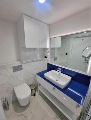 A modern bathroom with a white toilet, a blue sink vanity, and a large mirror. - Fantastic 1-bedroom apartment with AC Panoramic View (Batumi)