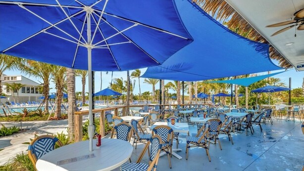 An outdoor pool area with blue umbrellas, lounge chairs, and tables. - CT 7344 Pond and Fountain View Condo - Welcome to Paradise (Fort Pierce)