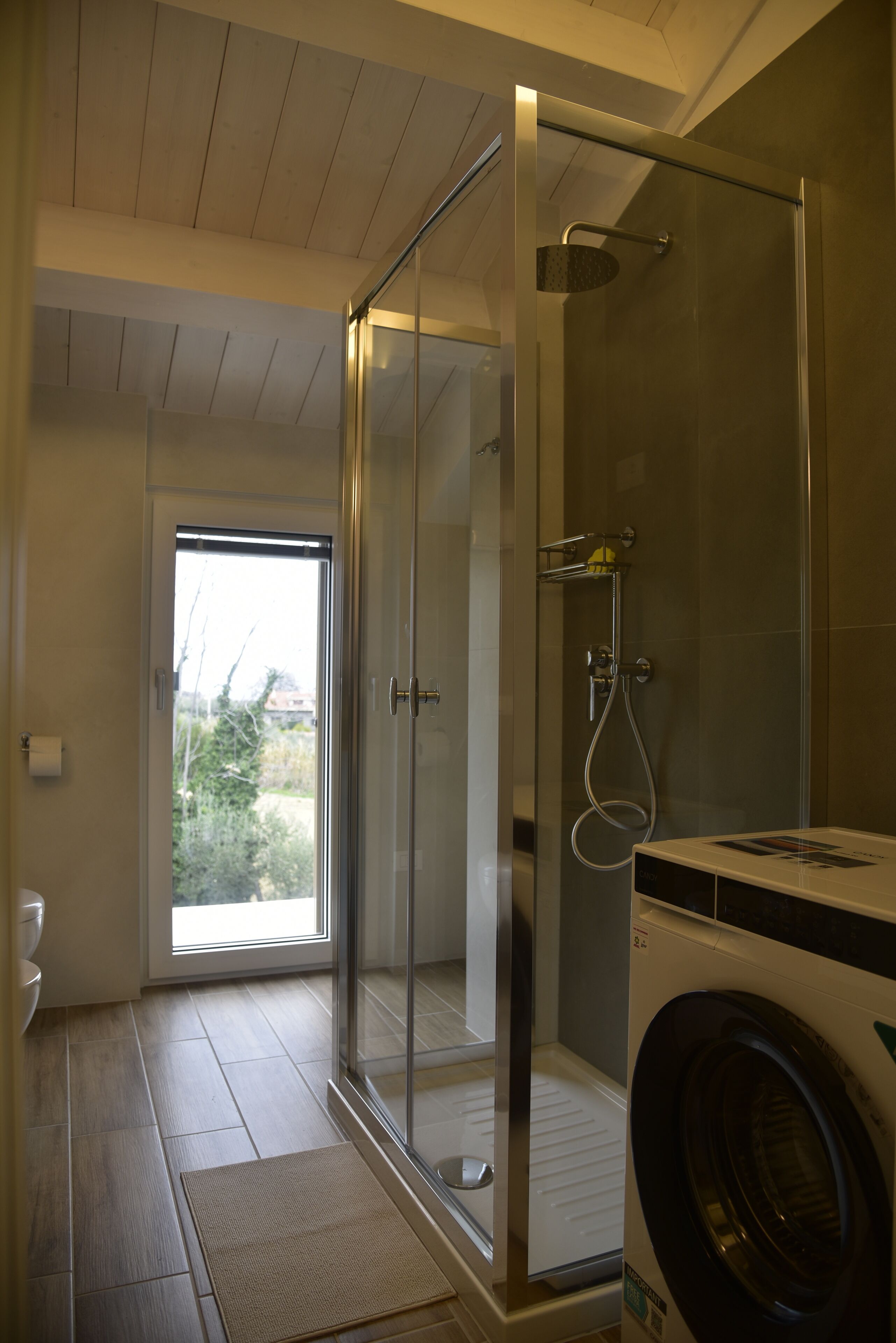 Une salle de bain moderne dotée d’une douche à parois de verre, d’un lave-linge encastré et offrant une vue à travers la porte en verre.