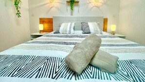 Una cama bien hecha con ropa de cama estampada, dos lámparas de noche y luces fijadas a la pared.
