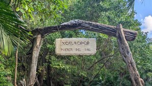 A wooden archway with a sign reading "Xcalacoop Puerta del Sol" leading to a stone pathway surrounded by trees. - Eco Resort with 1-bedroom hotel suite in charming Playa del Carmen with AC (Playa del Carmen)