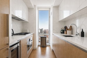 Een moderne keuken met marmeren aanrechtbladen, roestvrijstalen apparatuur en een stadszicht door een groot raam.