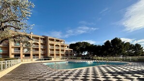 Hotel amb zona de piscina, terra amb quadres i un edifici gran amb balcons.