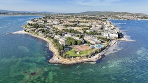 Vista aèria d'una vila costanera amb una illa central que presenta edificis residencials, un camp esportiu i un far.
