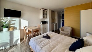Habitació d'hotel amb llit, escriptori amb cadira, petita cuina i televisió penjada a la paret.