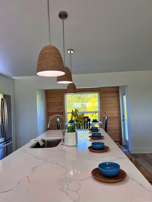 A modern kitchen with a central island, pendant lighting, and a view of greenery outside. - Bay view home w/private hot tub, 2 real desks & fenced yard. 31+ night stays (Oldsmar)