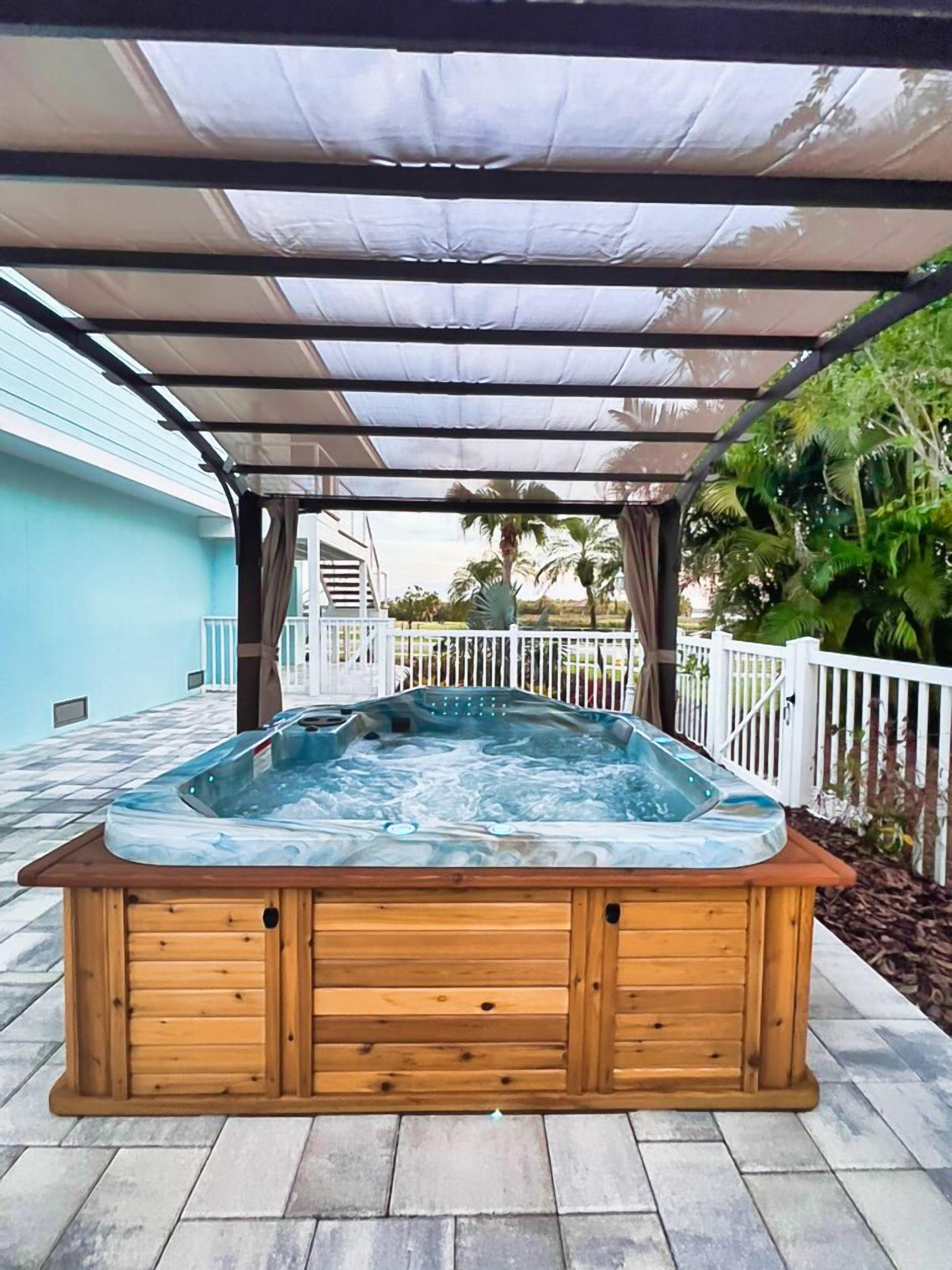 A hot tub under a pergola with a view of a house and palm trees.