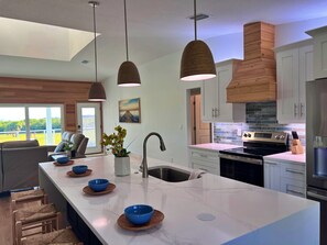 A modern kitchen with a central island, pendant lights, and a view of the outdoors. - Bay view home w/private hot tub, 2 real desks & fenced yard. 31+ night stays (Oldsmar)