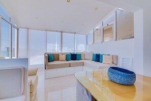 A modern living room with a sofa, a coffee table, and a large window offering a city view. - Carteia Beachfront at Praia da Gaivota (Quarteira)