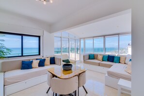 Una sala de estar moderna con ventanas amplias, un conjunto de sofás y una mesa de comedor.