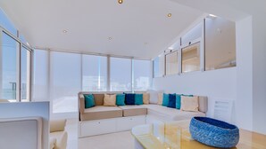 A modern living room with a sofa, a coffee table, and a large window offering a city view. - Carteia Beachfront at Praia da Gaivota (Loulé)