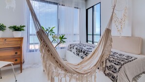 A bedroom with a hammock bed, a wooden dresser, and a large window with sheer curtains. - Carteia Beachfront at Praia da Gaivota (Loulé)