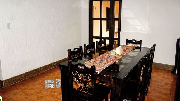 Un comedor con una larga mesa de madera, seis sillas y un mantel con diseño.