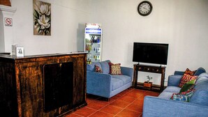 Una sala de estar con un mueble de madera, sofás azules, un televisor y un refrigerador.
