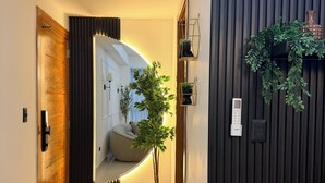 Un pasillo moderno con una puerta de madera, una planta en maceta y una lámpara de pared.